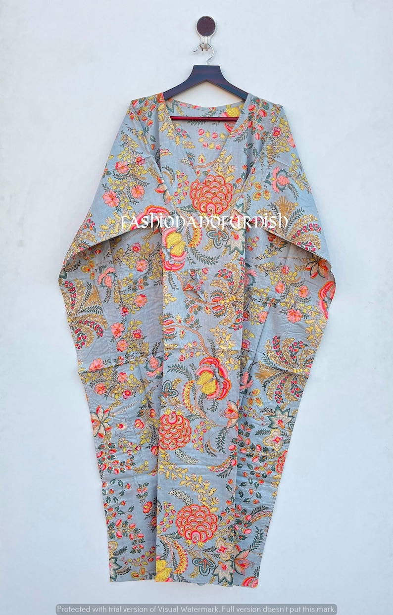 Puede incluir: Un vestido kaftan gris con estampado floral, colgado de una percha de madera. El vestido tiene cuello en V y presenta un dise&ntilde;o de flores y hojas rojas, amarillas y rosas. El texto "FASHIODADOFURDISH" es visible en el vestido.