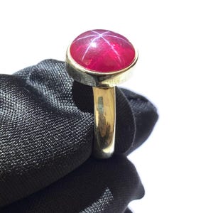 Op de afbeelding: Een gouden ring met een grote, ronde, rode ster-robijn edelsteen.