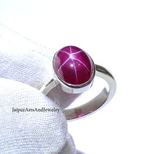 Può includere: Un anello d'argento con una pietra preziosa di rubino stella rosso. Il rubino ha un motivo a forma di stella al centro.