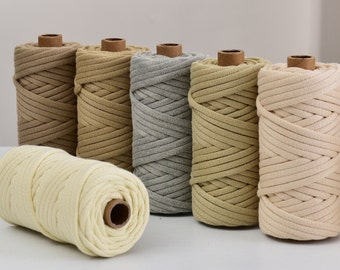 May include: A collection of six spools of thick, braided cotton cord in various neutral colors, including cream, beige, gray, and brown. The spools are cylindrical with a cardboard core, suitable for macrame and crafting projects.