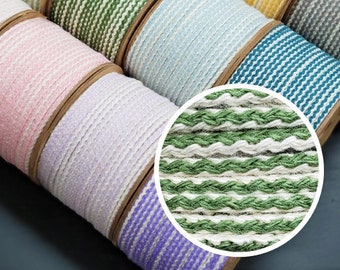 May include: Spools of colorful woven ribbon in various shades, including green, blue, yellow, and pink. The ribbon has a textured, striped pattern. The spools are arranged in a diagonal row, showcasing the variety of colors and textures.