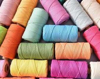 May include: A collection of colorful macrame cord spools in various shades, including yellow, orange, pink, green, and blue. The spools are arranged closely together, showcasing the vibrant colors and textures of the cord. The image is well-lit, highlighting the details of the yarn.