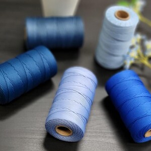 Peut inclure: Plusieurs bobines de fil bleu de différentes nuances, du bleu clair au bleu marine foncé. Les bobines cylindriques ont un cœur en carton, montrant le fil étroitement enroulé. L'image est bien éclairée, mettant en valeur les différentes teintes.