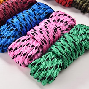 May include: Close-up of several coiled ropes in various colors, including blue, pink, and green. Each rope has a black diamond pattern. The ropes are arranged on a white surface, showcasing their vibrant hues and textures.