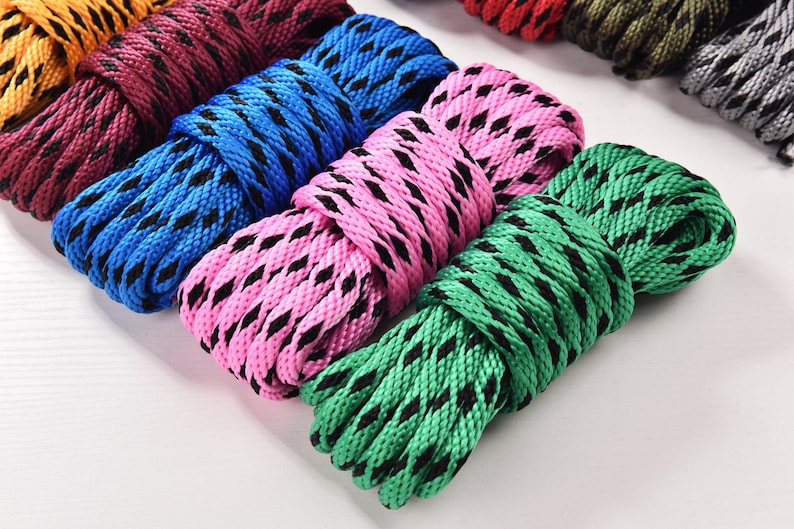 May include: Close-up of several coiled ropes in various colors, including blue, pink, and green. Each rope has a black diamond pattern. The ropes are arranged on a white surface, showcasing their vibrant hues and textures.