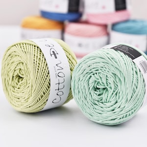 May include: A selection of colourful cotton yarn skeins, including shades of green, pink, and blue. Each ball of yarn is tightly wound with a label that reads "Cotton De". Suitable for various craft projects like knitting and crochet.