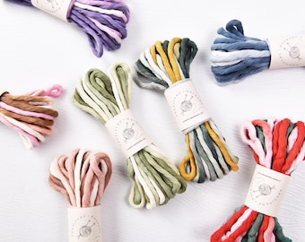 May include: Bundles of colorful macrame cord in various shades, including purple, pink, green, blue, and red. Each bundle is wrapped with a paper label that reads "KNOTILDE + MACRAME" and "A HAPPY HANDMADE LIFE". The cords are arranged on a white surface.