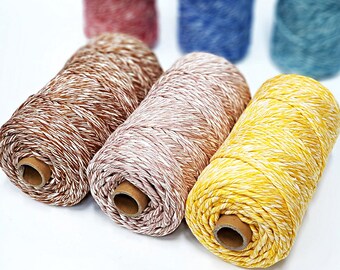 May include: Close-up of several spools of colorful twine. The twine is a mix of colors, including brown, pink, and yellow, with white accents. The spools are cylindrical and made of cardboard. The twine is likely used for crafting or packaging.