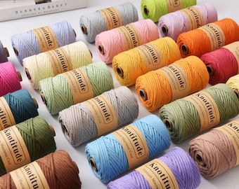 May include: An assortment of colorful macrame cord spools. Each spool is labeled with the brand name "Knotitude" and is available in a variety of colors, including pink, green, orange, and blue. The spools are arranged on a white surface.
