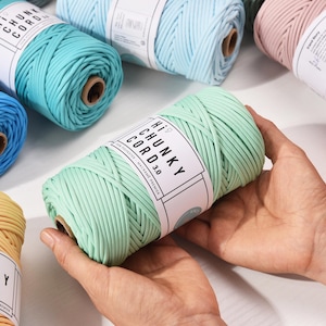 Op de afbeelding: Een verzameling kleurrijke spoelen dik garen in pasteltinten, waaronder blauw, turquoise, roze en geel. De spoelen zijn voorzien van het label "Hi Chunky Cord 3.0". De afbeelding benadrukt de textuur en kleuren van het garen.
