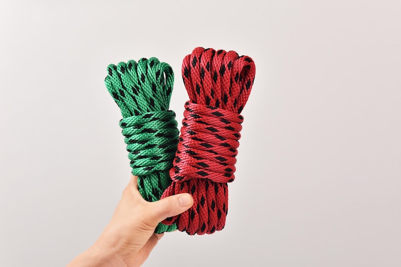 May include: Two coiled ropes, one green and one red, each with a black diamond pattern. The ropes are held against a white background, showcasing their texture and color contrast.