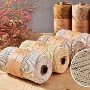 Op de afbeelding: Spoelen macramé koord in diverse neutrale kleuren, waaronder beige, bruin en grijs. Elke spoel is verpakt met een bruin papieren label met de tekst "brounte". Een close-up toont de geweven textuur van het koord. Ideaal voor knutselen.