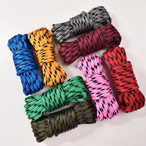 May include: A collection of colorful rope bundles in various shades, including blue, yellow, green, pink, red, and gray. Each bundle is tightly coiled, showcasing a textured pattern. The ropes are arranged on a white surface.