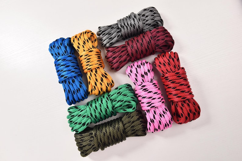 May include: A collection of colorful rope bundles in various shades, including blue, yellow, green, pink, red, and gray. Each bundle is tightly coiled, showcasing a textured pattern. The ropes are arranged on a white surface.