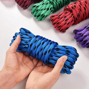 May include: A close-up of several colorful ropes. A blue rope with black accents is held in the center. Other ropes in red, green, purple, and yellow are visible in the background. The ropes are tightly coiled.
