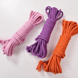 Puede incluir: Tres madejas de cuerda en tonos rosa, morado y naranja sobre un fondo blanco. Las cuerdas están bien enrolladas, con extremos sueltos. La imagen está bien iluminada, resaltando la textura y los colores de la cuerda. Ideal para manualidades.