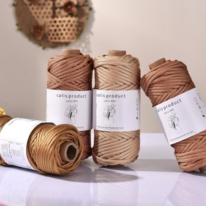 Può includere: Sono mostrate diverse bobine di corda marrone e beige. Ogni bobina ha un'etichetta con la scritta "calis product calis 905". La corda è avvolta attorno ad anime di cartone. Sullo sfondo un elemento decorativo da parete e un piccolo ombrellino di carta.