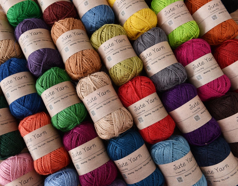 May include: A collection of colorful jute yarn balls, each wrapped with a brown paper label that reads "Jute Yarn". The yarn is available in various colors, including green, red, blue, and brown. Ideal for weaving, dry craft, and macrame projects.
