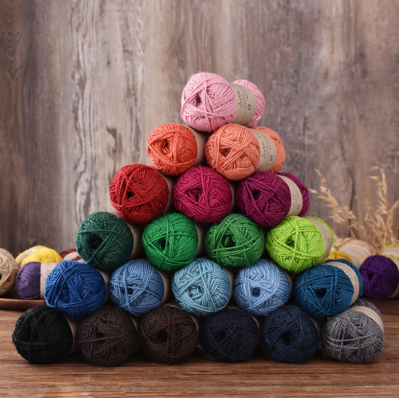 May include: A pyramid of colorful yarn balls in various shades, including pink, orange, red, green, blue, and black. The yarn is arranged on a wooden surface with a wooden backdrop, creating a visually appealing display for crafting projects.