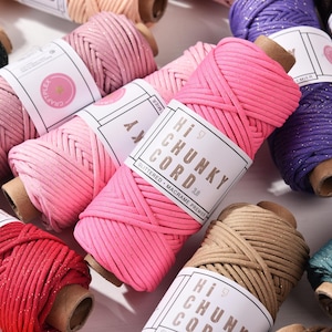 May include: A selection of colourful macramé cord spools. The spools are in shades of pink, red, purple, green, and brown. Each spool has a label that reads "Hi Chunky Cord" and "Glittered Macrame Premier".