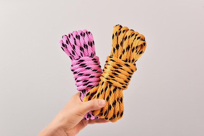 May include: Two bundles of rope, one pink and one yellow, each with a black diamond pattern. The ropes are held together, showcasing their contrasting colors and textures. The image is set against a plain background.