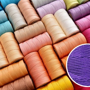 Può includere: Una collezione di rocchetti di filo colorati in varie tonalità, tra cui blu, beige, rosa, arancione, viola e rosso. Un inserto in primo piano mostra la trama del filo viola. Ideale per progetti di artigianato e cucito.