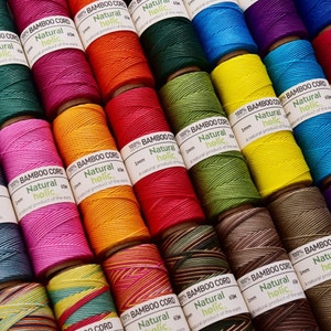 May include: A display of vibrant bamboo cord spools in a range of colours, such as pink, green, yellow, and purple. Each spool is labelled with "100% BAMBOO CORD Natural holic". The cord is 1mm thick and 65m long.