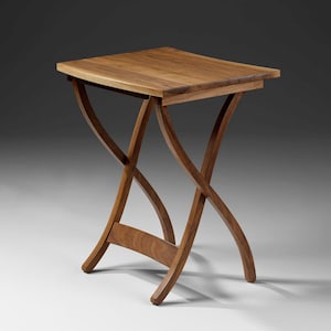 Puede incluir: Una pequeña mesa auxiliar de madera con una tapa cuadrada y patas curvas. La mesa está hecha de madera de color marrón claro y tiene un diseño simple y elegante. La mesa mide aproximadamente 51 cm de altura.