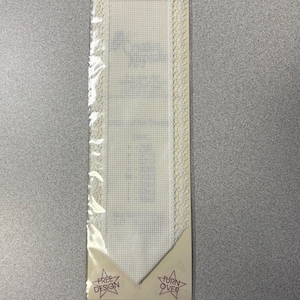 May include: A white Aida cloth bookmark with a lace border. The bookmark is packaged in a clear plastic bag with a brown card that says "PAGE POINTER" and "FREE DESIGN" and "TURN OVER".