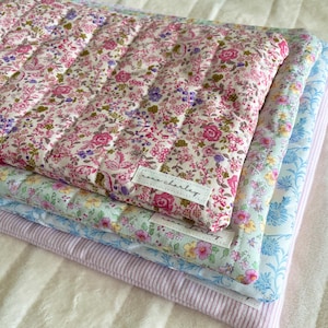 Puede incluir: Tres bolsas de tela acolchadas con estampados florales. La bolsa superior es rosa y blanca con una etiqueta que dice "rose charley". La bolsa del medio es azul claro y blanca con una etiqueta que dice "rose charley". La bolsa inferior es de rayas rosa y blancas.