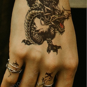 May include: A black and white temporary tattoo of a dragon on a person's hand.