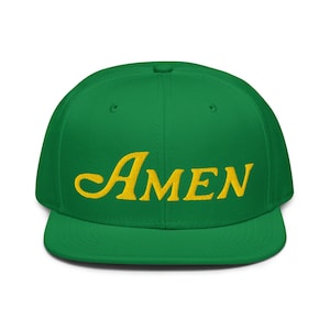 Può includere: Un cappellino da baseball verde con visiera piatta. La parola "AMEN" è ricamata in giallo, in corsivo, sulla parte anteriore. Il cappellino è di un colore verde acceso.