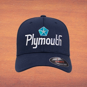 May include: A navy blue baseball cap with a white embroidered Plymouth logo and a blue and white star emblem. The cap has a Flexfit label on the back.