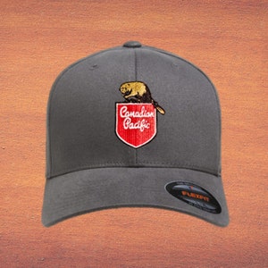 May include: A grey Flexfit baseball cap with a red and white embroidered patch displaying the words "Canadian Pacific" and a beaver illustration. The cap has a curved peak and a structured crown.