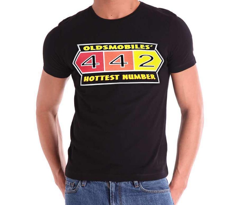 May include: A black short-sleeved t-shirt featuring a graphic print on the chest. The design includes the text OLDSMOBILES' 4 4 2 HOTTEST NUMBER in yellow, white, and black, with the numbers 4, 4, and 2 set against red, orange, and yellow backgrounds.