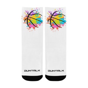 May include: A pair of white socks with a black basketball graphic on each sock. The basketball is surrounded by colourful paint splatters in shades of pink, yellow, blue, and green. The socks have black footbeds and the word "DUNTALK" is printed on the bottom of each sock.