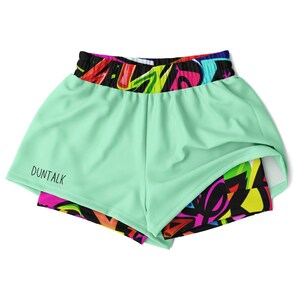 Puede incluir: Shorts deportivos de color verde menta con una cintura de estampado de graffiti colorido y un logotipo "DUNTALK" negro en la parte delantera.