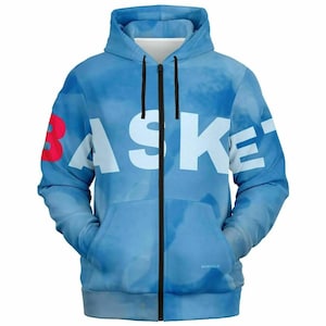 Peut inclure: Un sweat à capuche zippé bleu clair avec un motif nuageux et le mot BASKET imprimé en grandes lettres blanches sur la poitrine, la lettre B étant rouge. Le vêtement comprend une capuche avec des cordons noirs et une fermeture éclair noire.