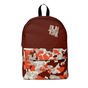 May include: A maroon backpack with a black handle and zipper. The top section is solid maroon, while the front pocket features a camouflage pattern in shades of orange, brown, and cream. The text "RUN TANK" is printed on the upper right.