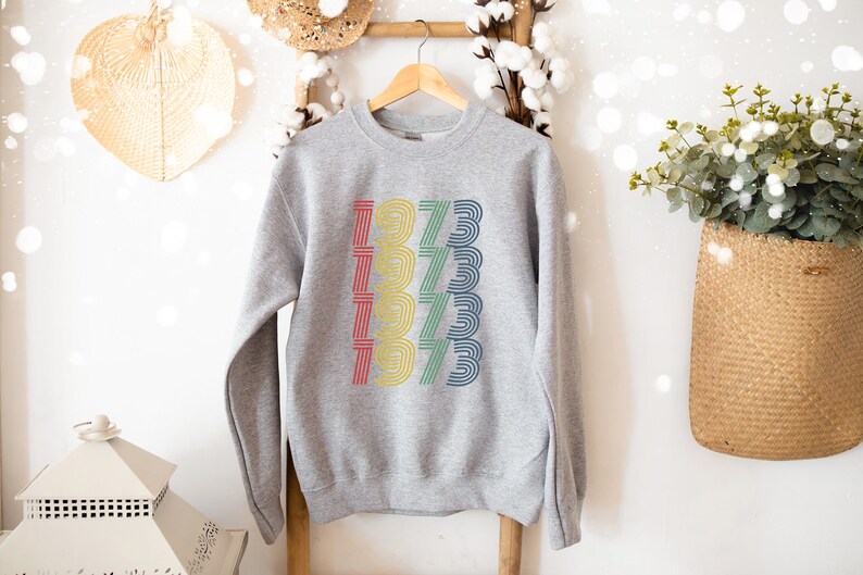 May include: Gray sweatshirt with a rainbow colored graphic of the year 1973 repeated five times.