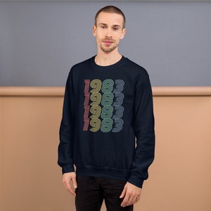 May include: A navy blue sweatshirt with a retro-style graphic of the year 1983 repeated in a rainbow of colors.