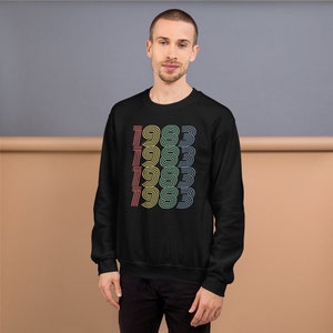 May include: Black sweatshirt with a rainbow colored graphic of the year 1983 repeated five times.