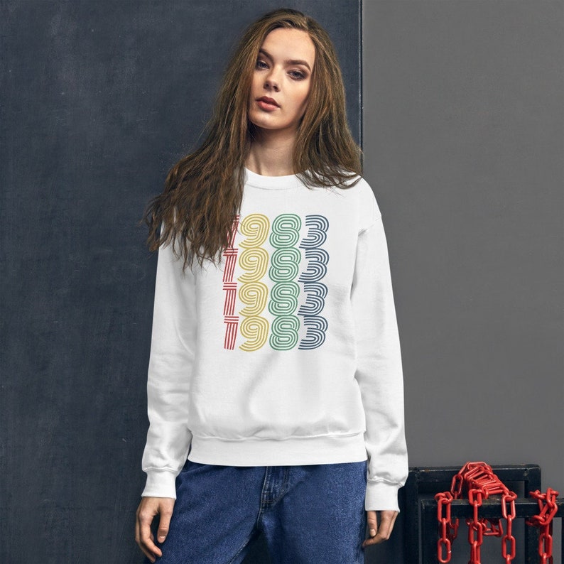 May include: White sweatshirt with a colorful graphic of the year 1983 repeated five times.