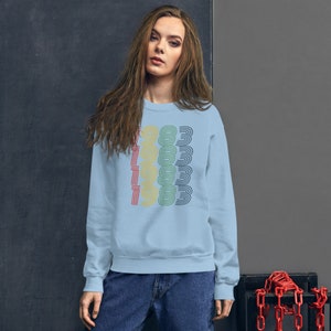 May include: A light blue sweatshirt with a retro-style graphic of the year 1983 in rainbow colors.