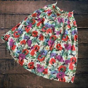 Könnte beinhalten: Ein Rock mit floralem Muster mit cremefarbenem Hintergrund, verziert mit roten, lila und blauen Blumenmustern. Der Rock hat ein plissiertes Design und ist aus leichtem Stoff gefertigt. Der Rock ist im Vintage-Stil.