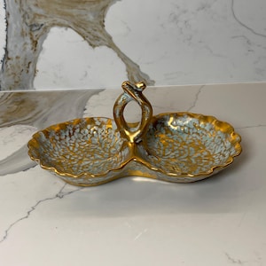 Könnte beinhalten: Ein zweiteiliges, goldfarbenes Serviertablett mit Griff. Die Schale hat ein hellblaues und goldenes Blumenmuster auf der Innenseite. Der Rand und der Griff sind goldfarben. Die Schale ist wahrscheinlich aus Keramik oder Porzellan.