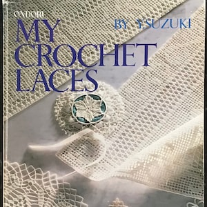 May include: A book titled "My Crochet Laces" by Y. Suzuki. The cover features a close-up of various white crochet lace patterns. The title is in blue, with the author's name in a smaller font. A decorative pin is visible.