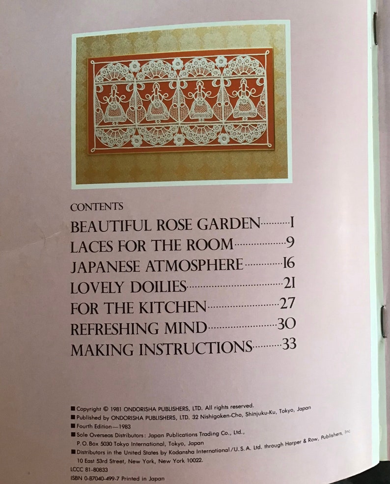 May include: A book page featuring a detailed illustration of white lace designs on a reddish-brown background. The image is framed within a gold border. The book's contents include topics like 'Beautiful Rose Garden' and 'Lovely Doilies'.