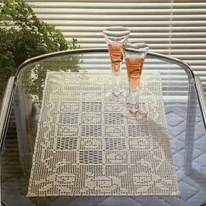 May include: A crocheted centerpiece, measuring 22 inches by 12 inches, is displayed on a glass table. Two stemmed glasses with a pink liquid sit atop the table. The text "Centerpiece" is visible.