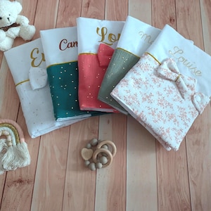 Peut inclure: Cinq livres en tissu pour bébé pliés avec des prénoms brodés dont Louise, présentant des sections blanches et des bases à motifs colorés avec de petits nœuds. Inclut un ours en peluche blanc, une suspension arc-en-ciel et un anneau en bois.